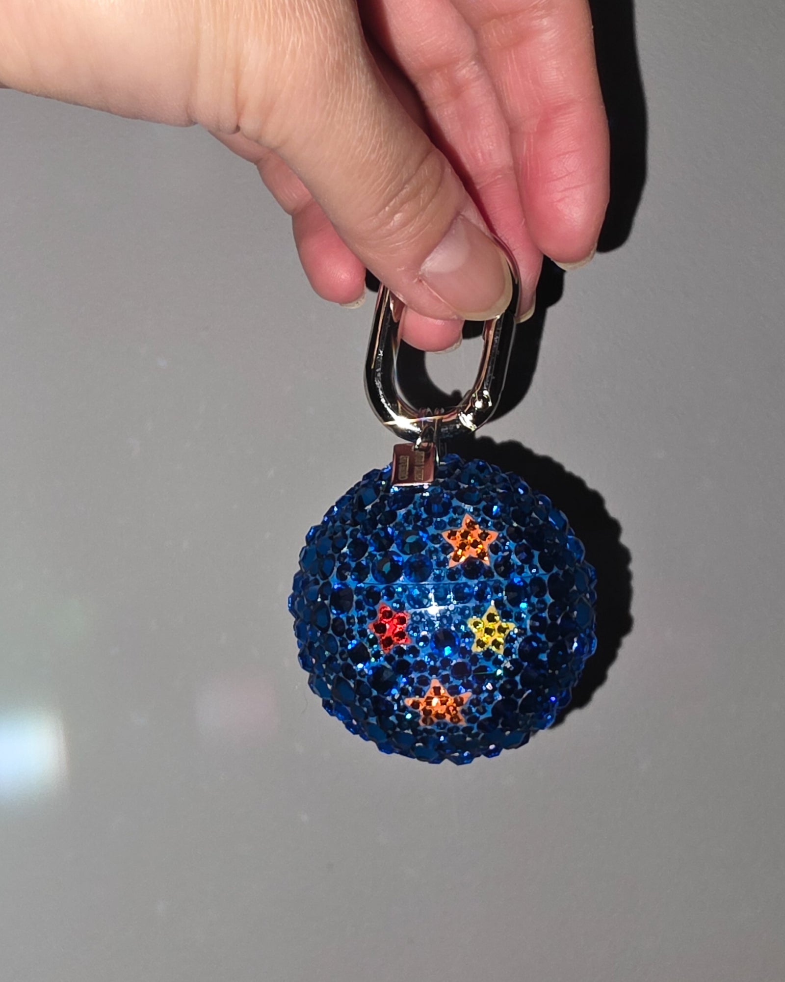 Blue glittery keychain with colorful stars held by a hand against a gray background