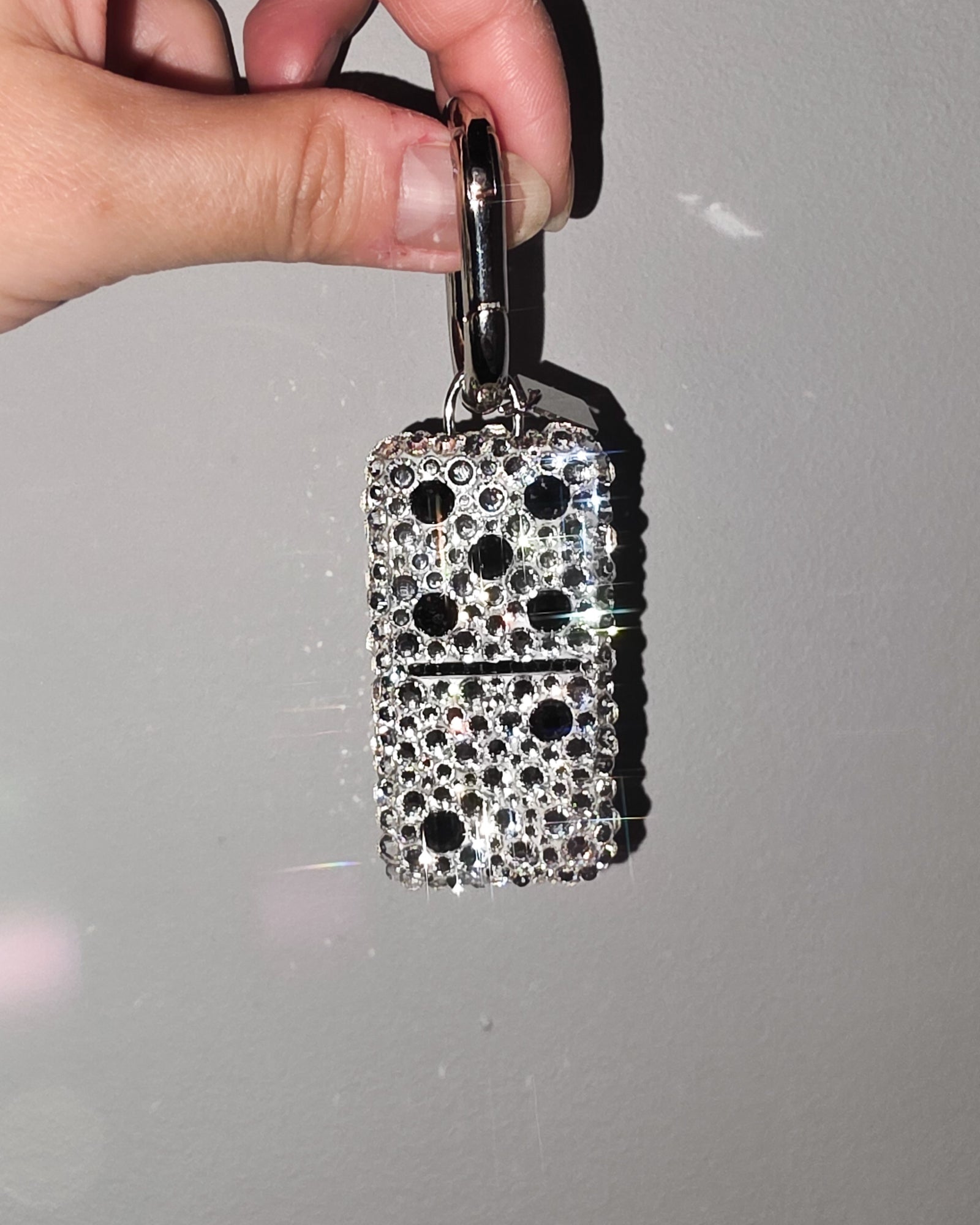 Hand holding a 5:2, fully rhinestoned domino bag charm against a gray background.