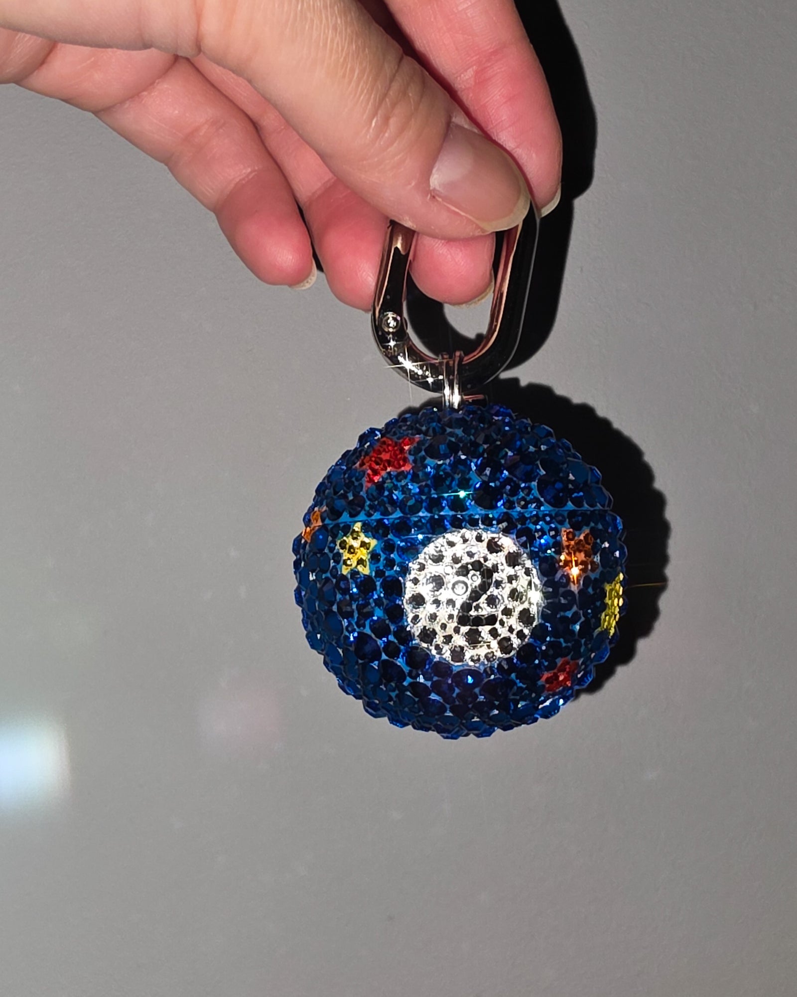 Keychain with blue ball and colorful star accents held by a hand against a gray background