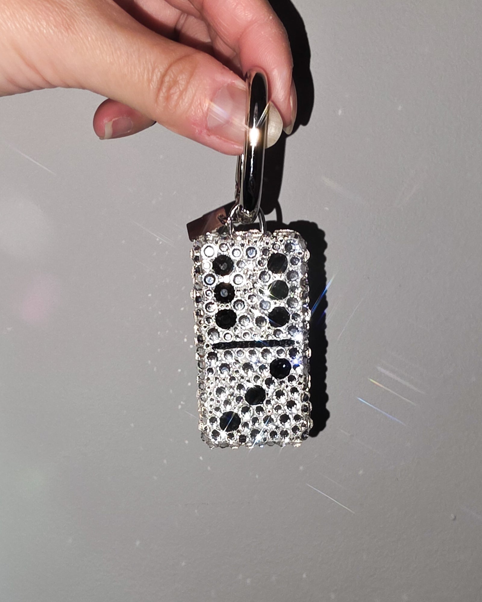 Hand holding a 6:3, fully rhinestoned domino bag charm against a gray background.