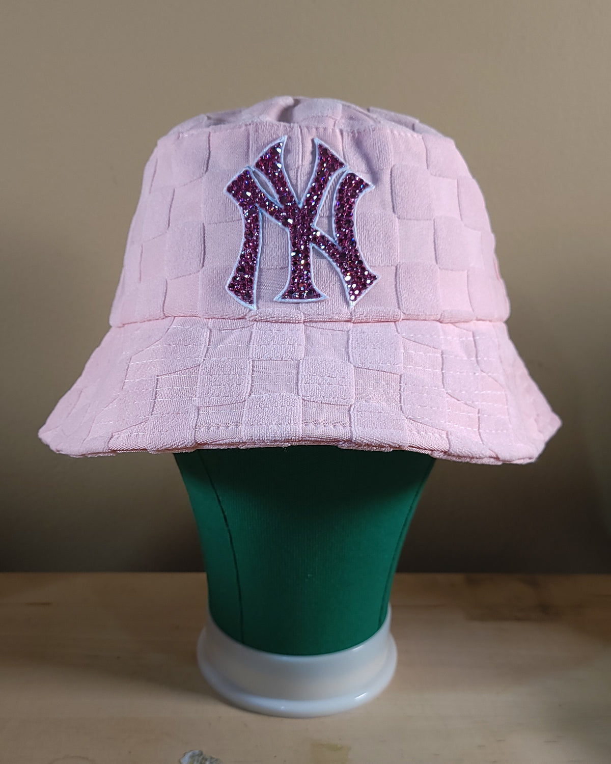 Front of NYC Barbie Bucket Hat, featuring a pink, checkered bucket hat with a pink logo covered in pink rhinestones.