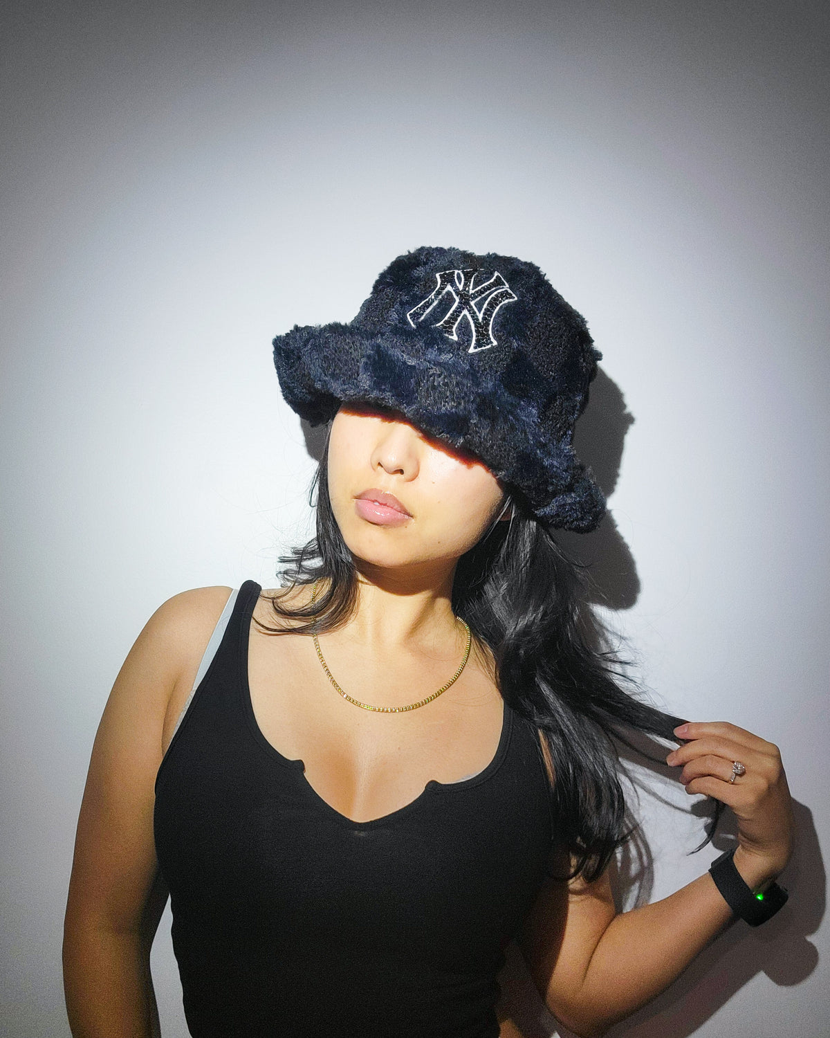 A furry, black, checkered bucket hat featuring a black logo covered in rhinestones, on top of someone's head.