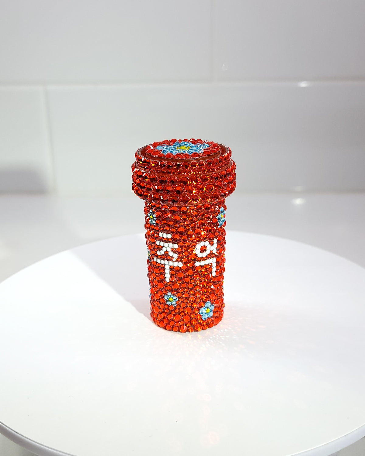 The front of the Chueok Pill Bottle, a fully rhinestoned pill bottle with prominent hangul in white, and small blue forget-me-not flowers scattered across. 