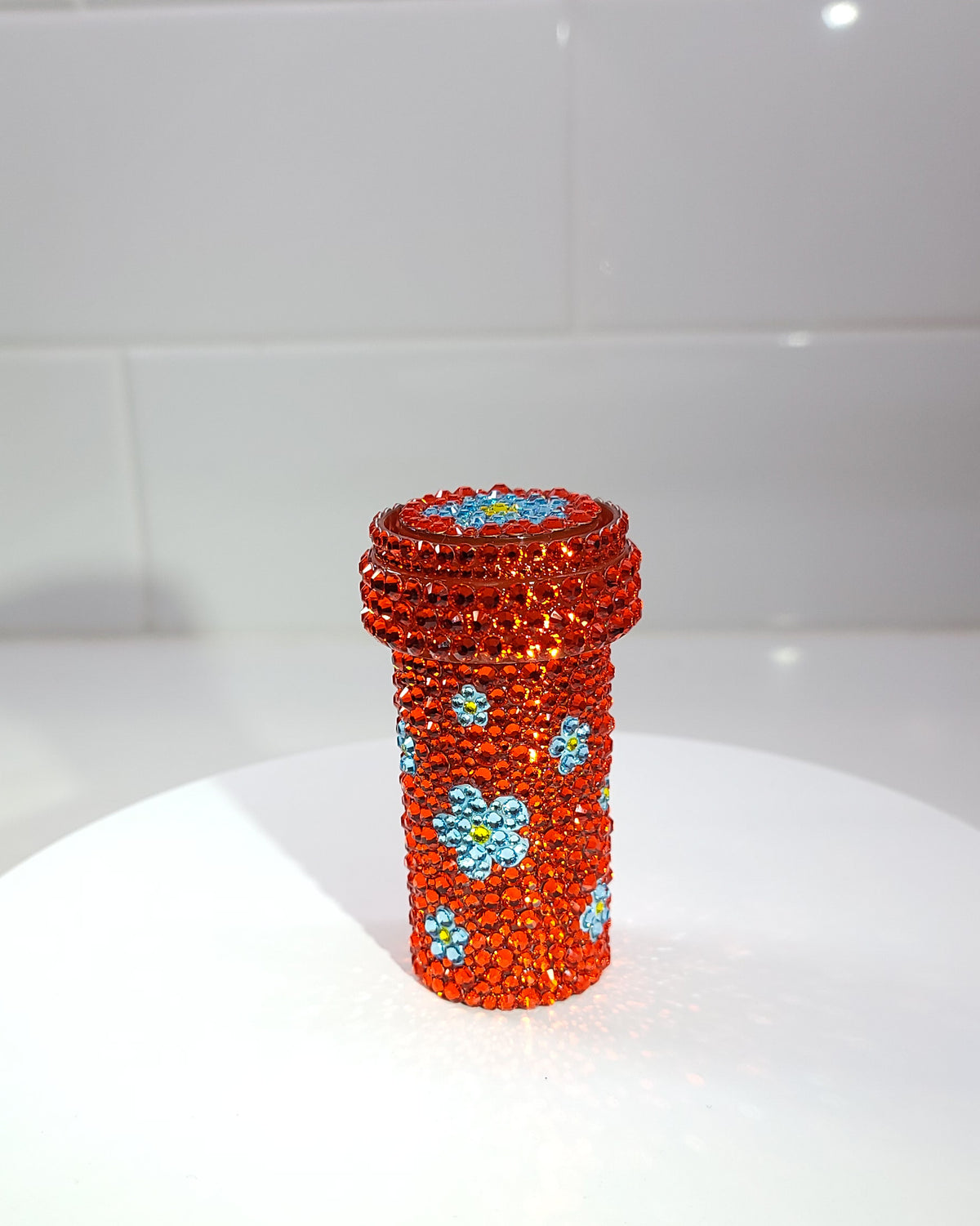 The backof the Chueok Pill Bottle, a fully rhinestoned pill bottle with small blue forget-me-not flowers scattered across. 