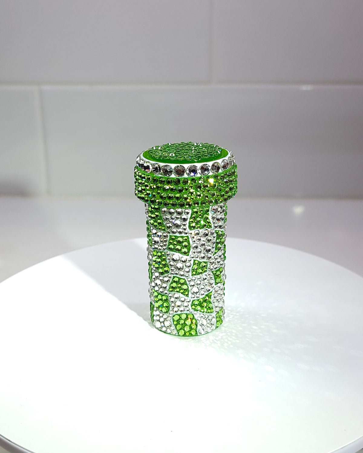 The front of the Trippy Checkerboard Pill Bottle, a fully rhinestoned pill bottle featuring a wavy checkerboard pattern with green and white as the two prominent colors.