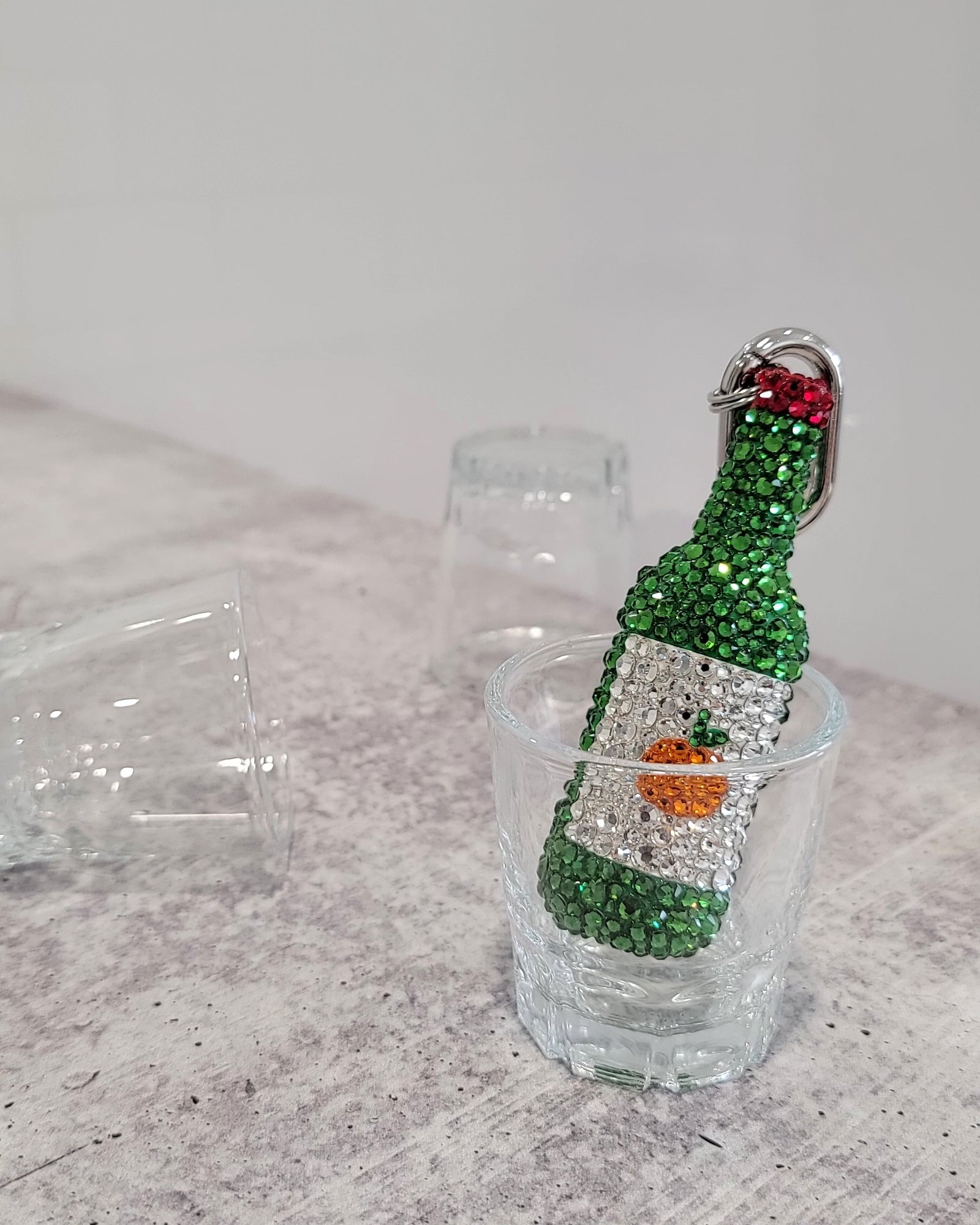 "Jeju Tangerine" Soju keychain (a green soju bottle with a white label and a small tangerine, featuring silver keychain hardware), sitting inside a soju cup.
