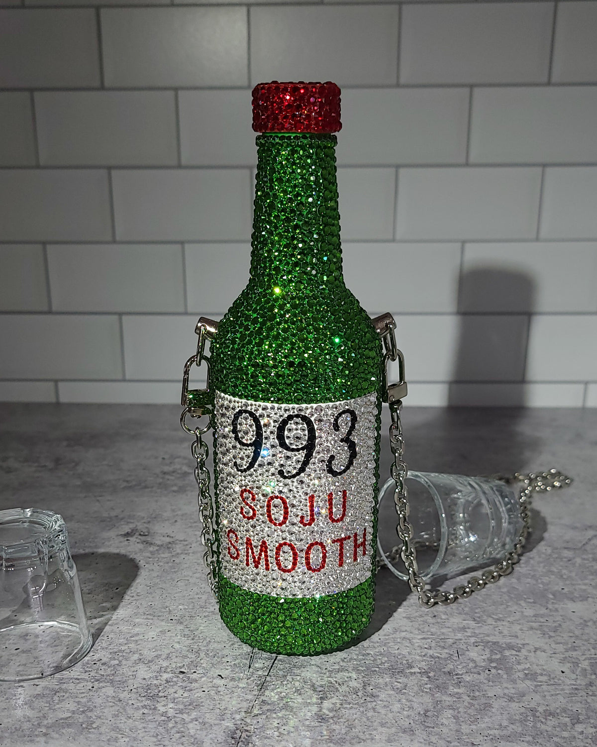 Fully rhinestoned SOJU purse on a flat surface, surrounded by soju cups.