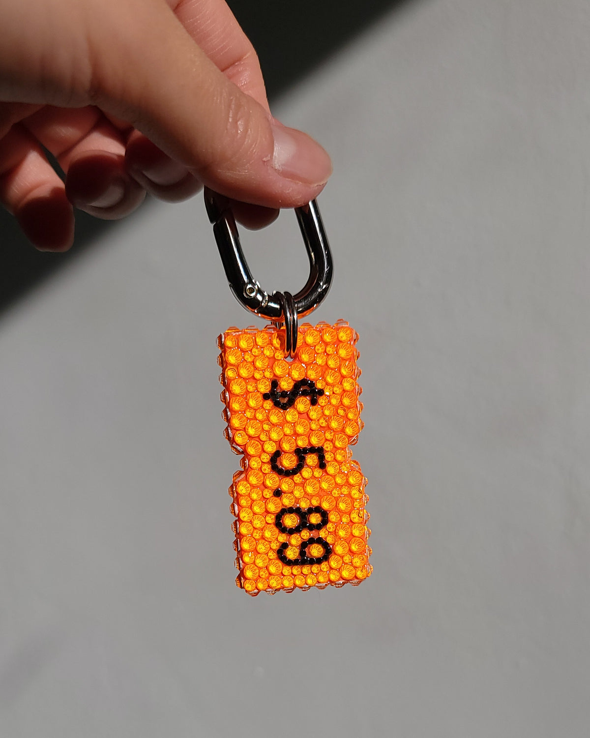 Front view of the Orange Price Tag Keychain, being held by hand against a gray background.
