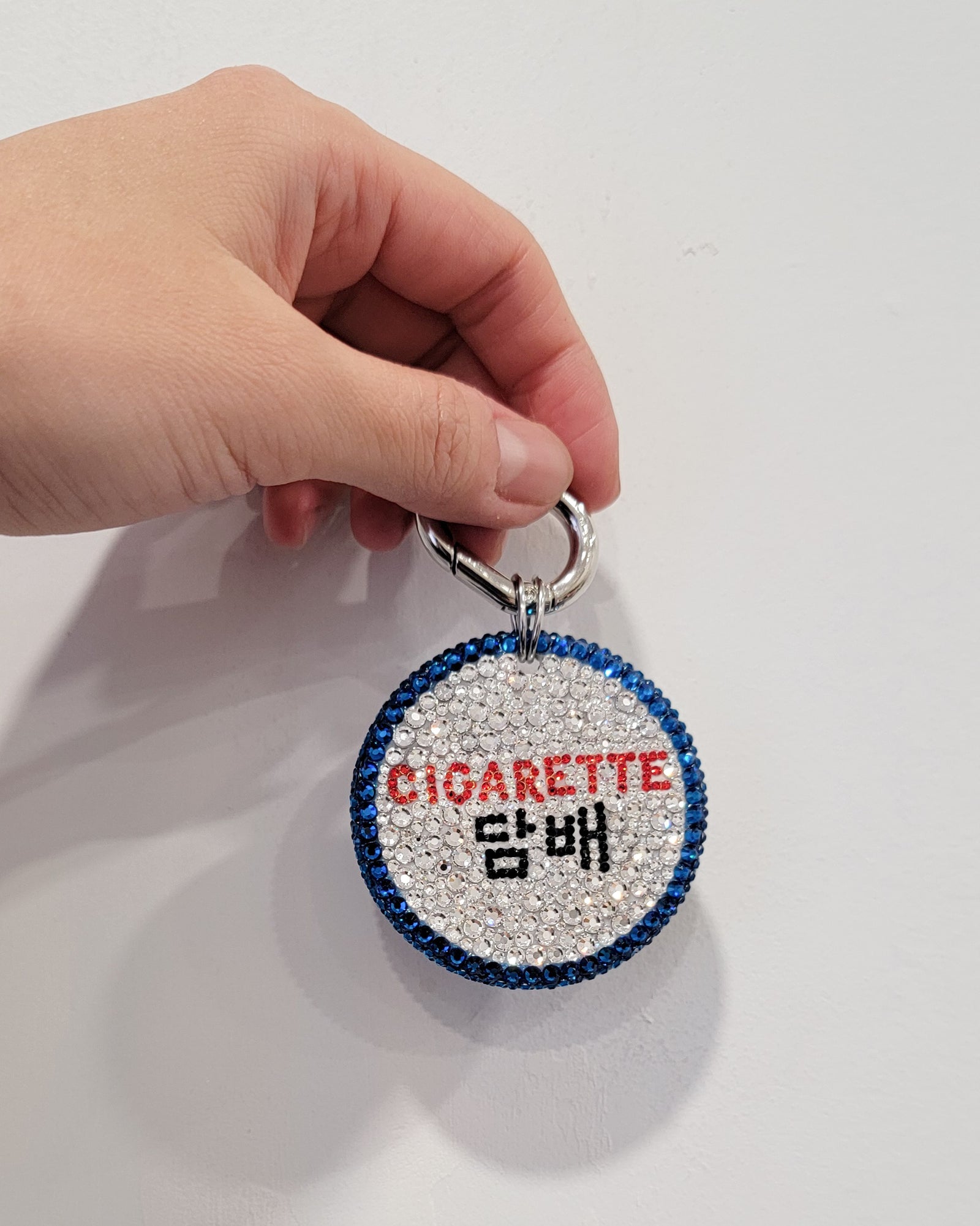 The Nightlife Cigarette Sign Bag Charm in low light, featuring prominent English in red, with hangul beneath in black.