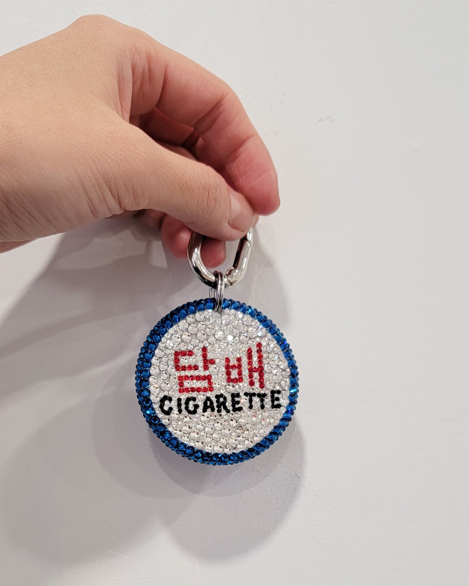 The Nightlife Cigarette Sign Bag Charm in low light, featuring prominent hangul in red, with English writing beneath in black.