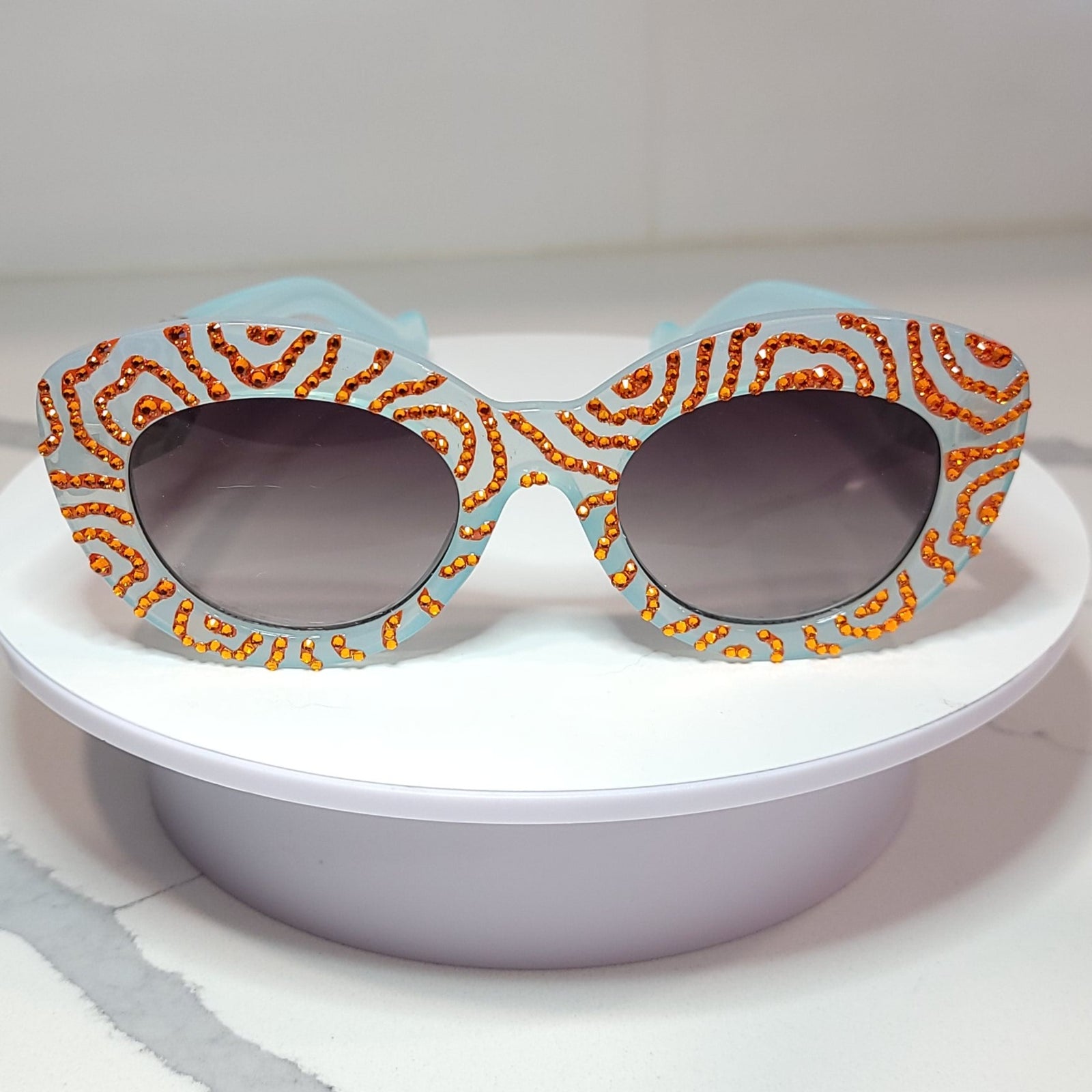 Acid Dreams Sunglasses Front, a pair of light blue sunglasses with handpainted orange swirls, and orange rhinestones.