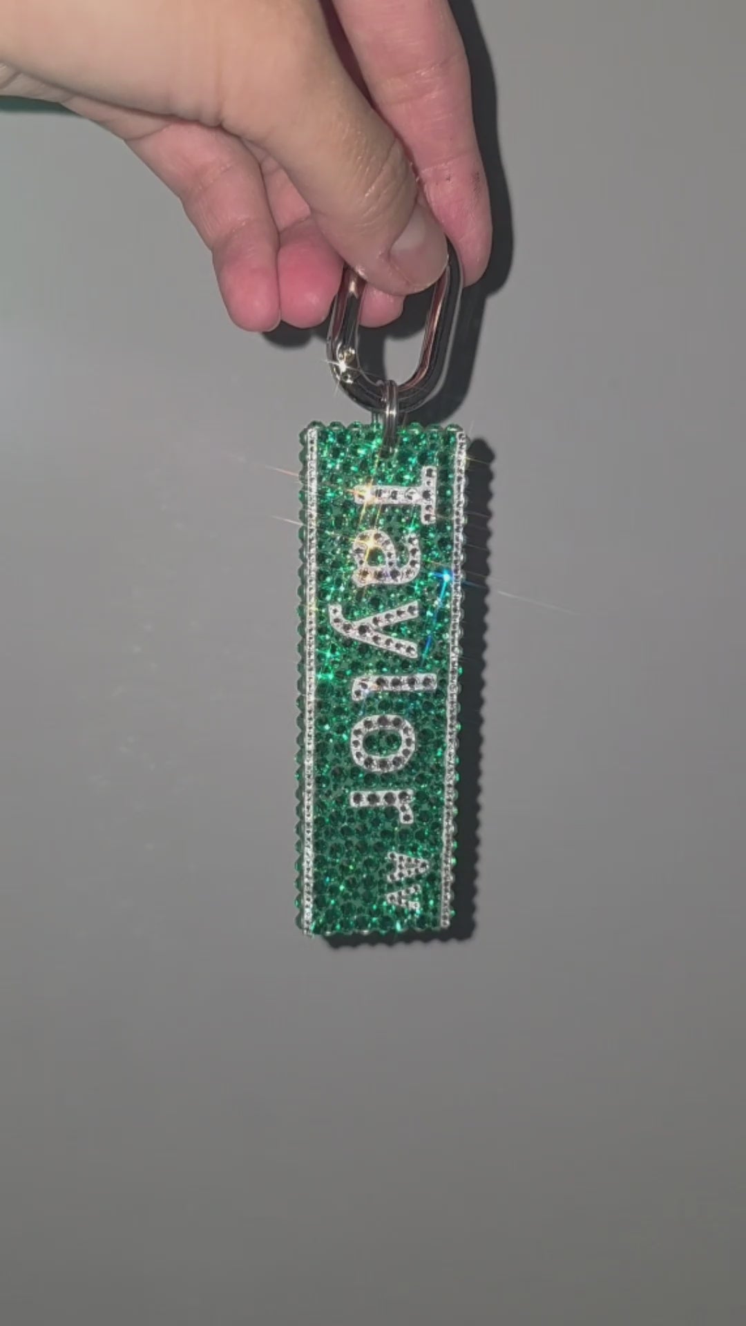 Video of a green street sign bag charm, covered in rhinestones, being slowly rotated in front of a gray background.