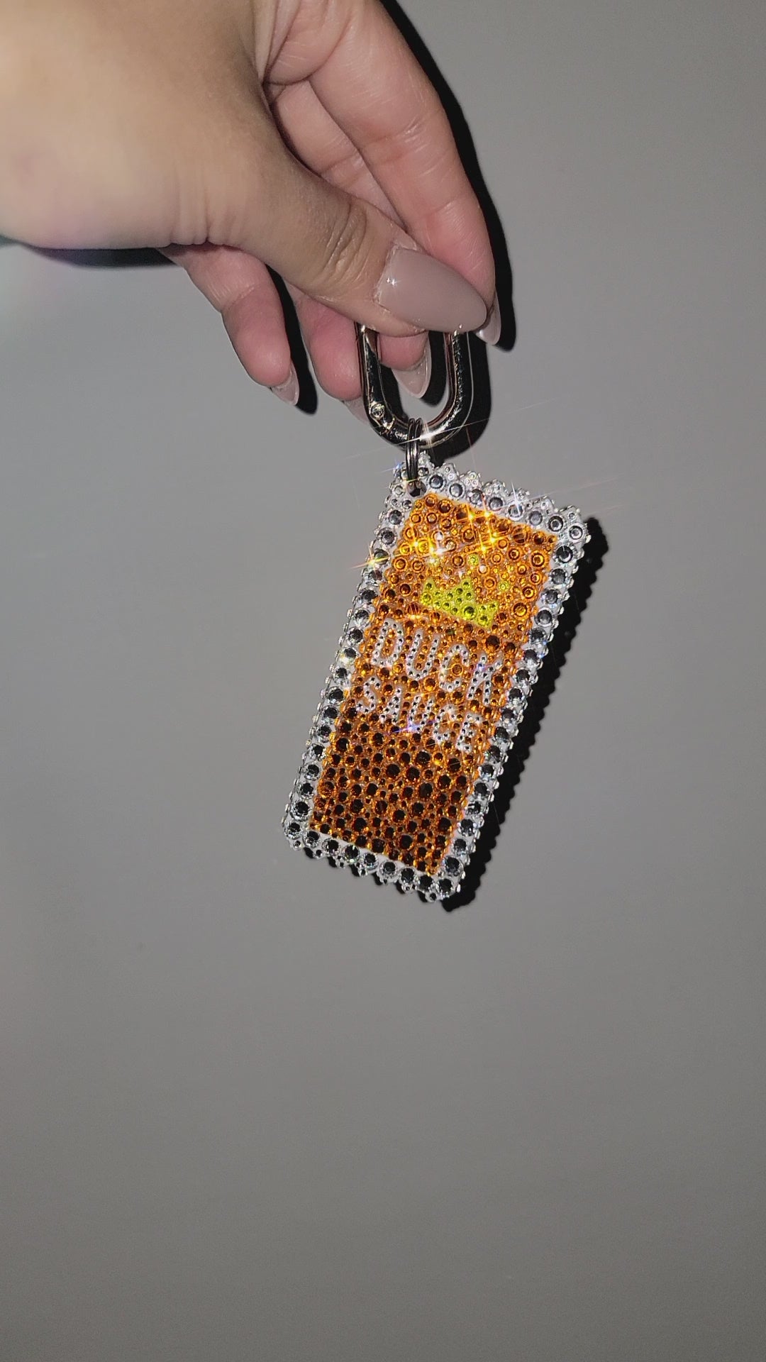Video of Duck Sauce Bag Charm being rotated by hand, against a gray background.