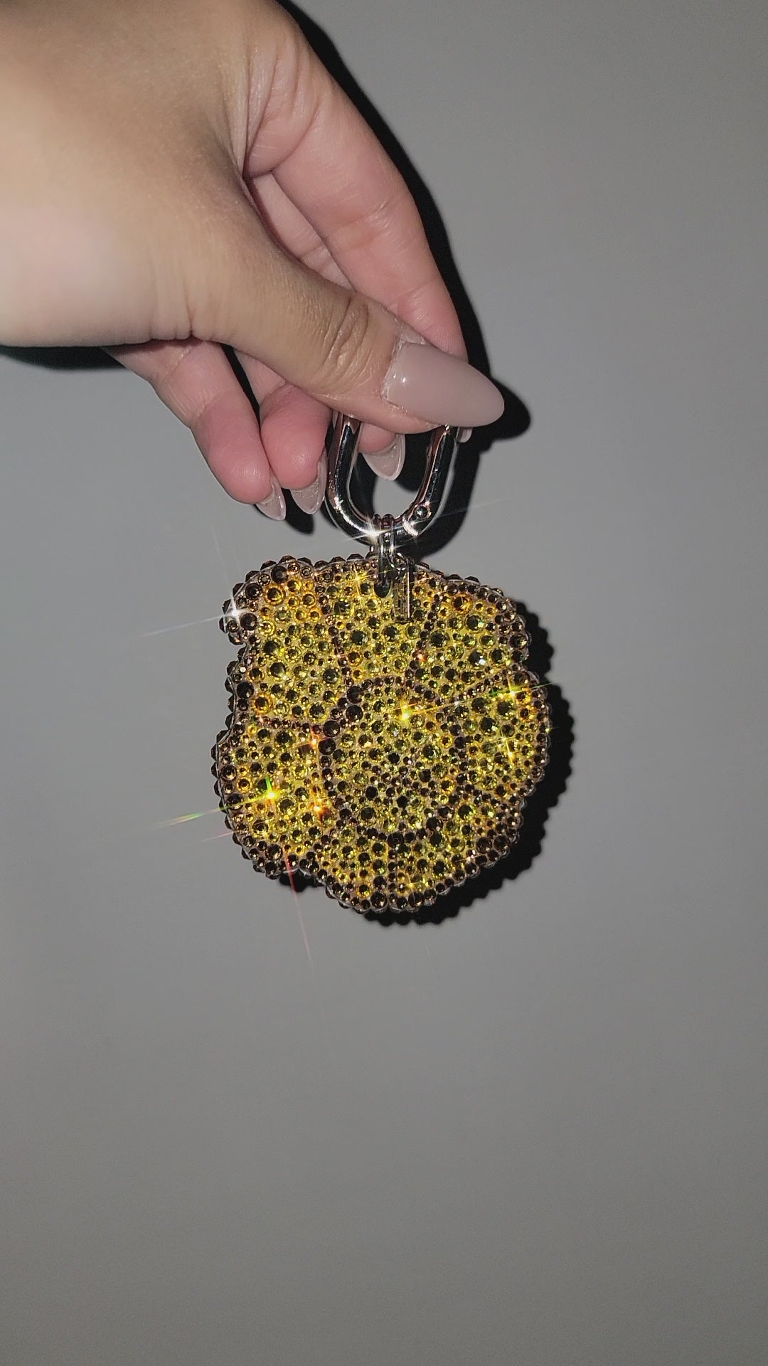 Video of Tostone Bag Charm rotating inside, being held by a hand against a gray background.