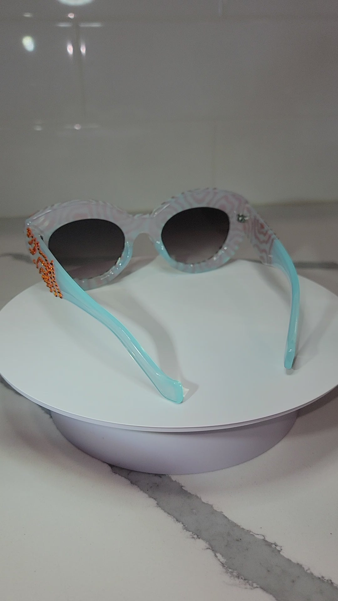 Acid Dreams Sunglasses VIdeo Inside Light, being rotated on a white surface, against a marble countertop.