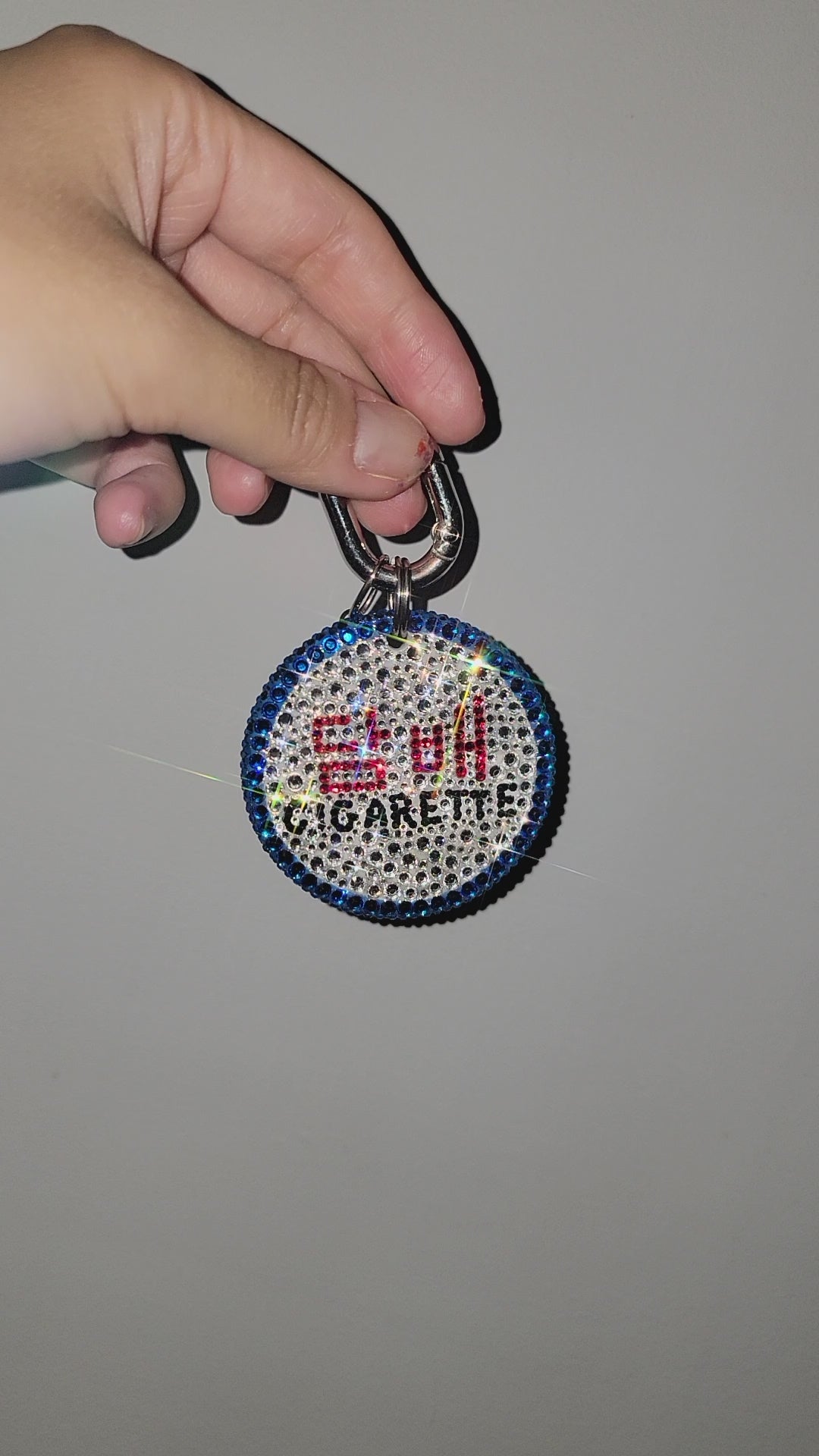 Video of Cigarette Bag Charm being rotated against a gray wall.