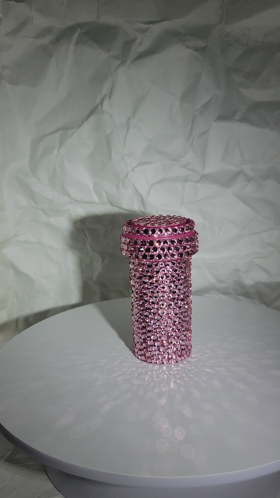 Video of the "MOM" Pill Case being rotated on a white surface, against a white, crumpled paper background.
