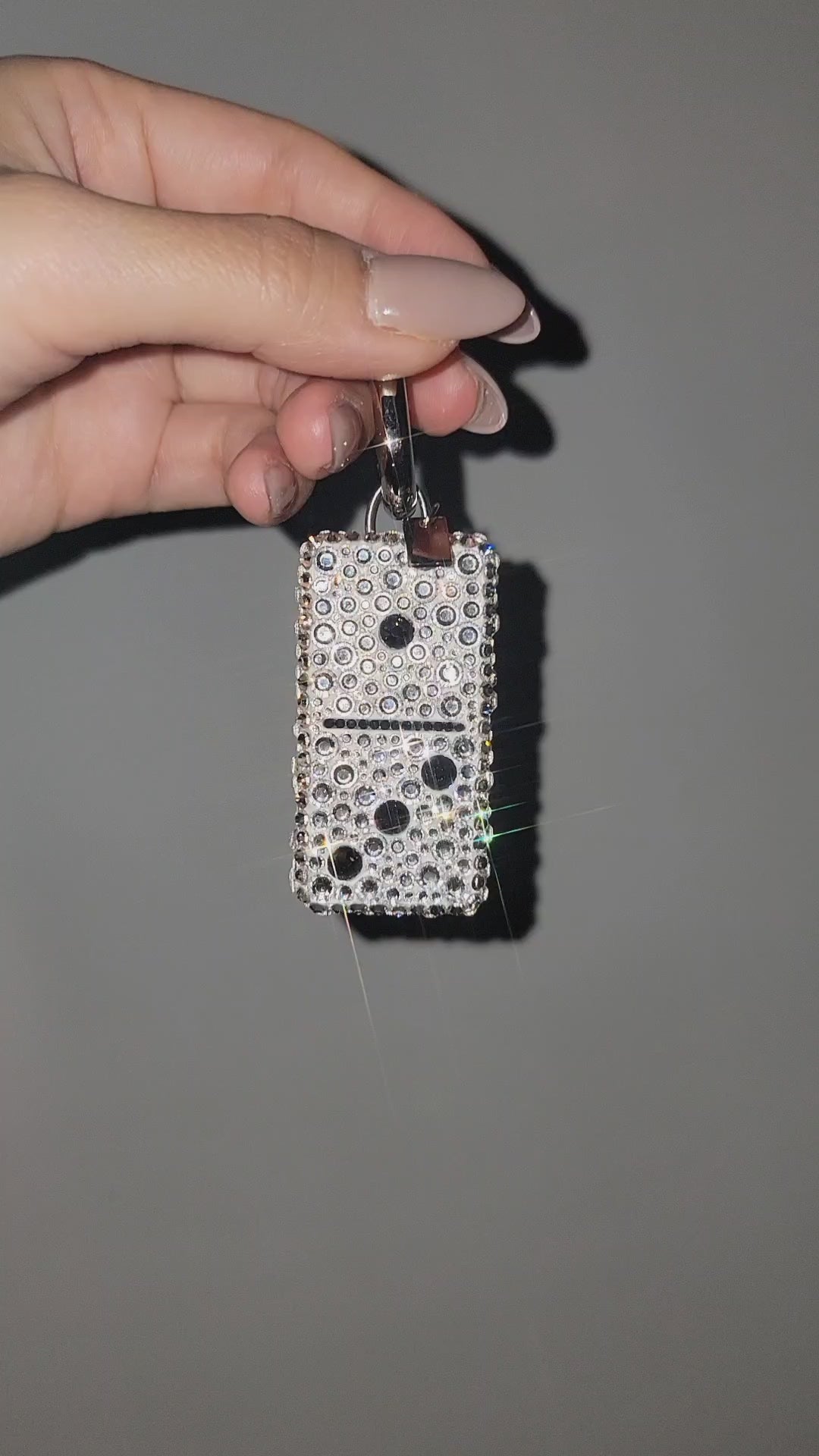 Video of Domino Bag Charm being rotated by hand against a gray background.