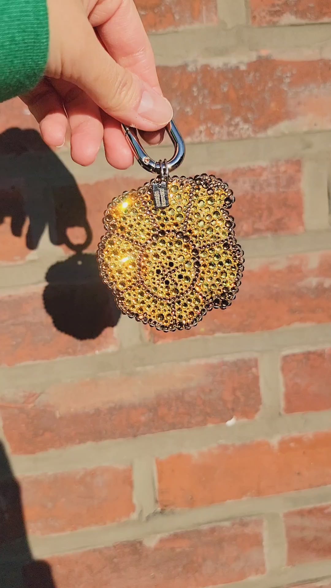 Video of Tostone Bag Charm in the sunlight, being held by a hand against a brick background.