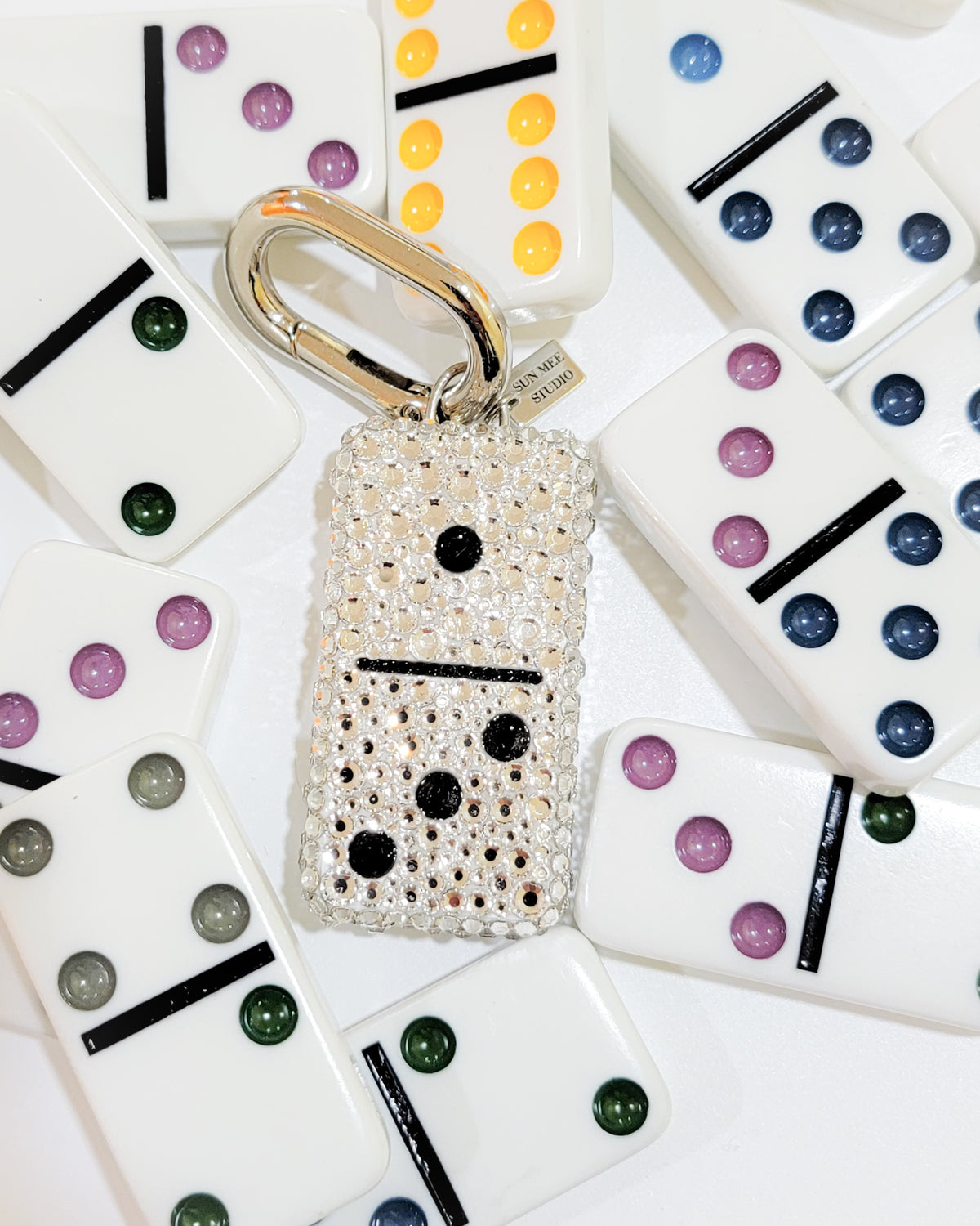 A 1:3, fully rhinestoned domino bag charm against a background of other dominoes.