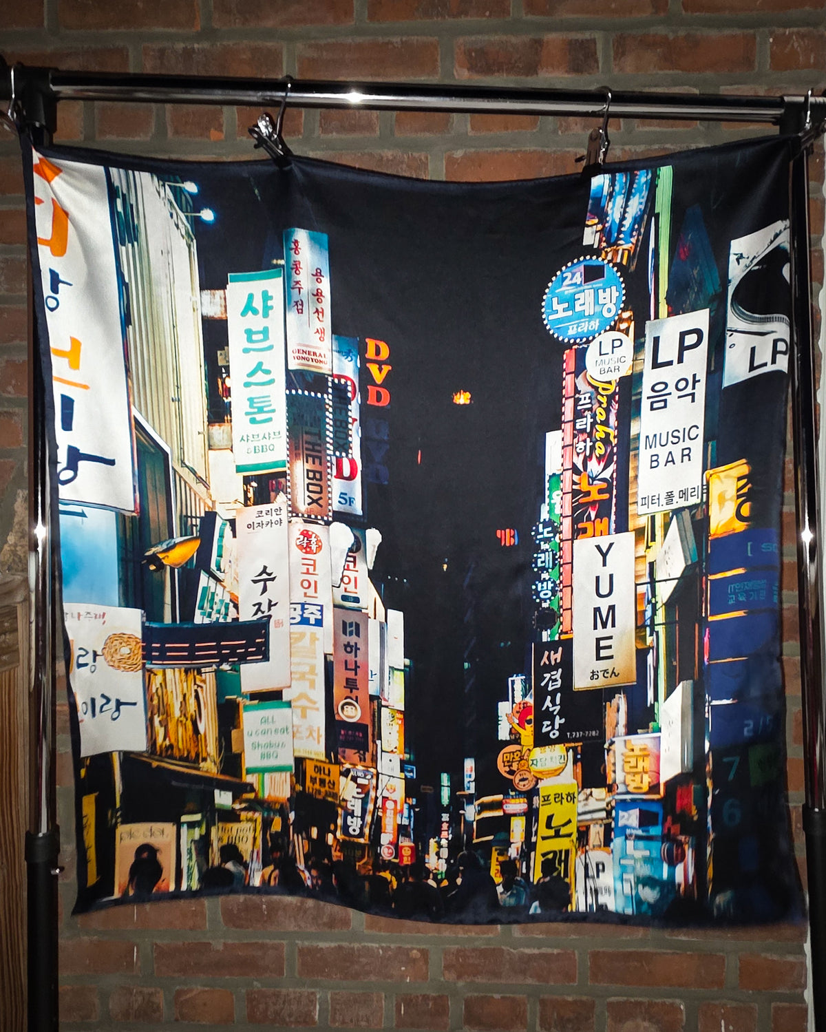 Fabric with colorful cityscape print hanging on a rod against a brick wall.