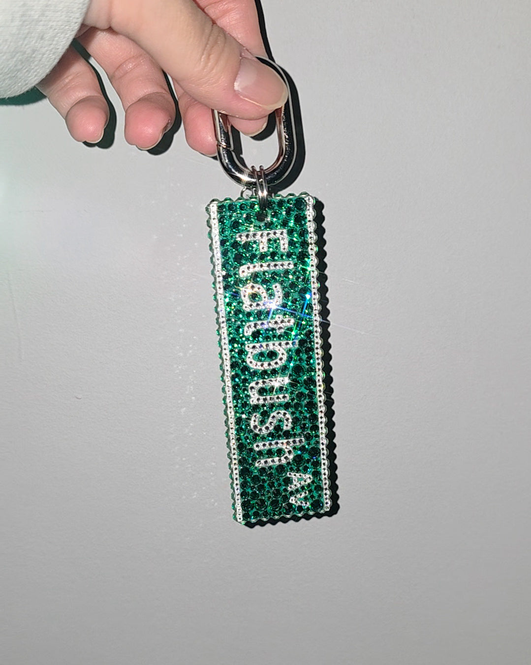 Green keychain with 'Flatbush' text held by a hand against a gray background