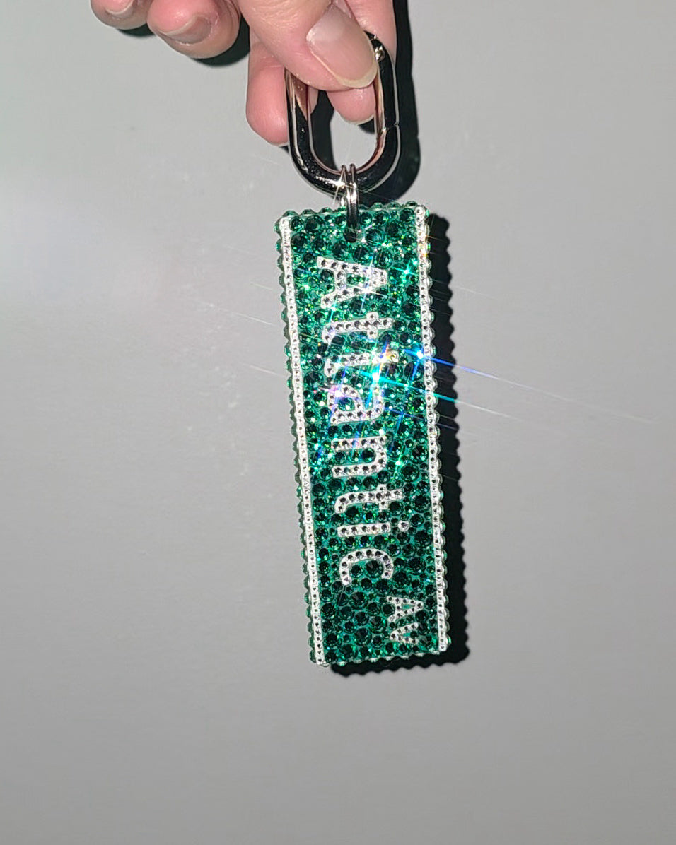 Green keychain with 'Atlantic' text held by a hand against a gray background