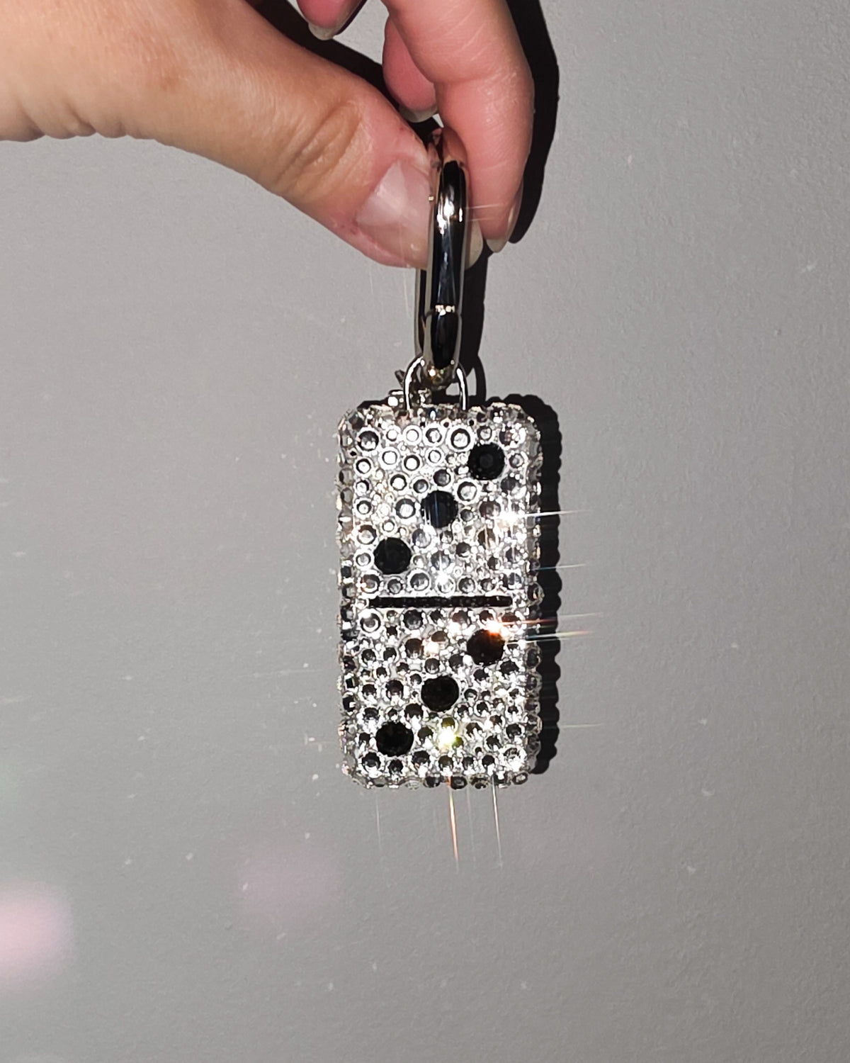 Hand holding a 3:3, fully rhinestoned domino bag charm against a gray background.