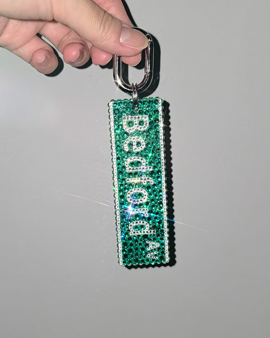 Green keychain with 'Bedford" text held by a hand against a gray background