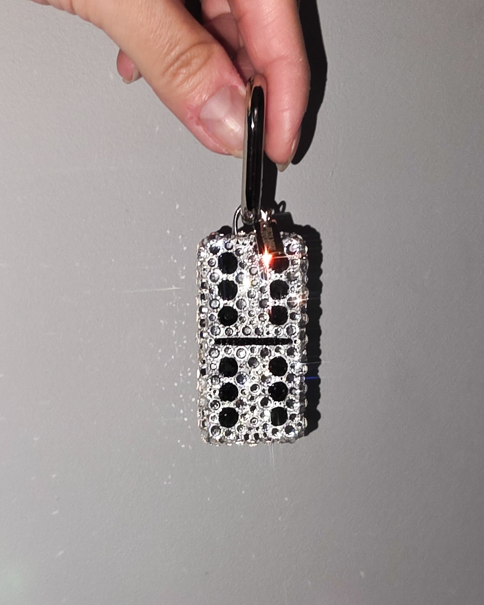 Hand holding a 6:6, fully rhinestoned domino bag charm against a gray background.