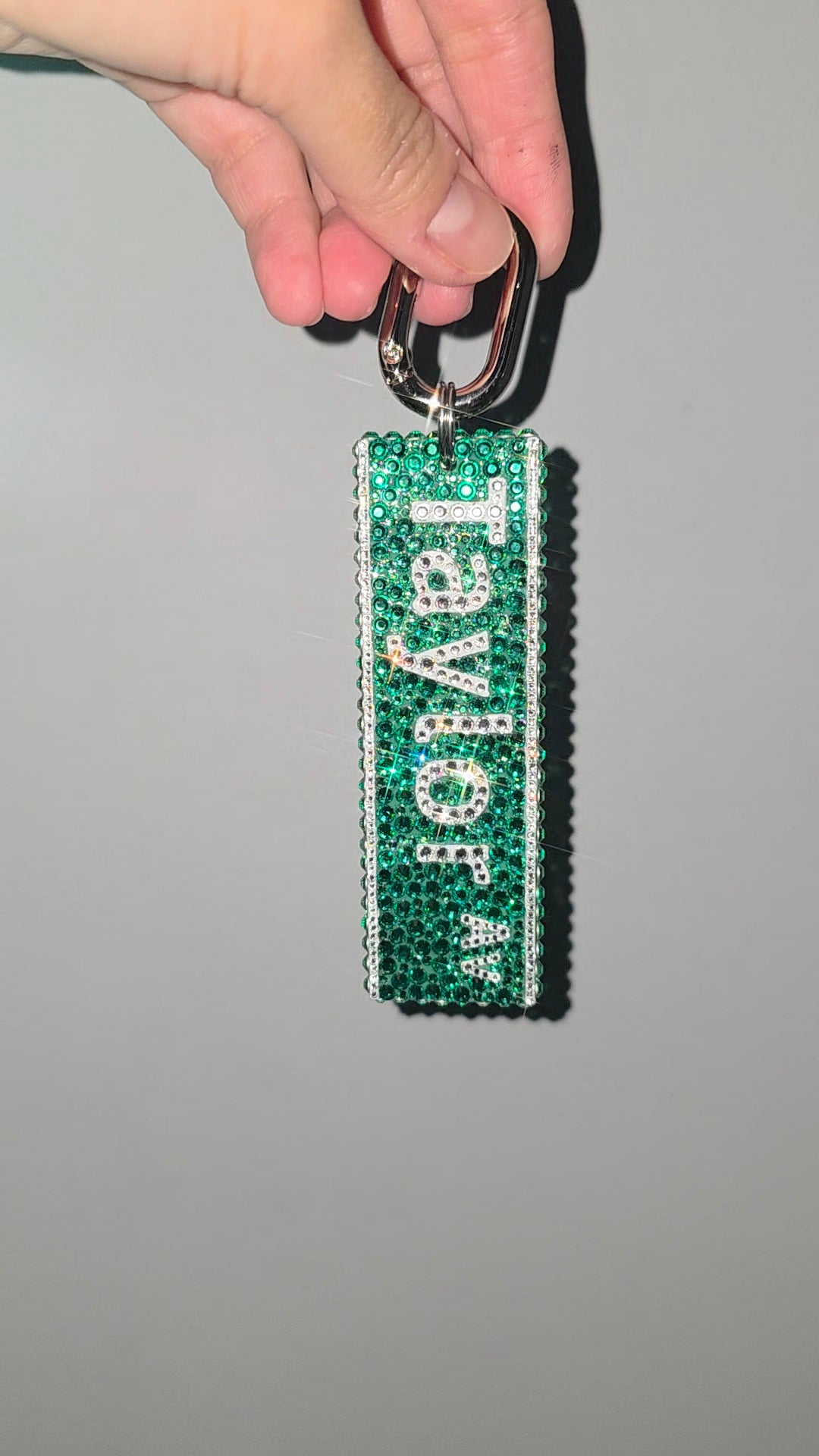 Green keychain with 'Taylor' text held by a hand against a gray background