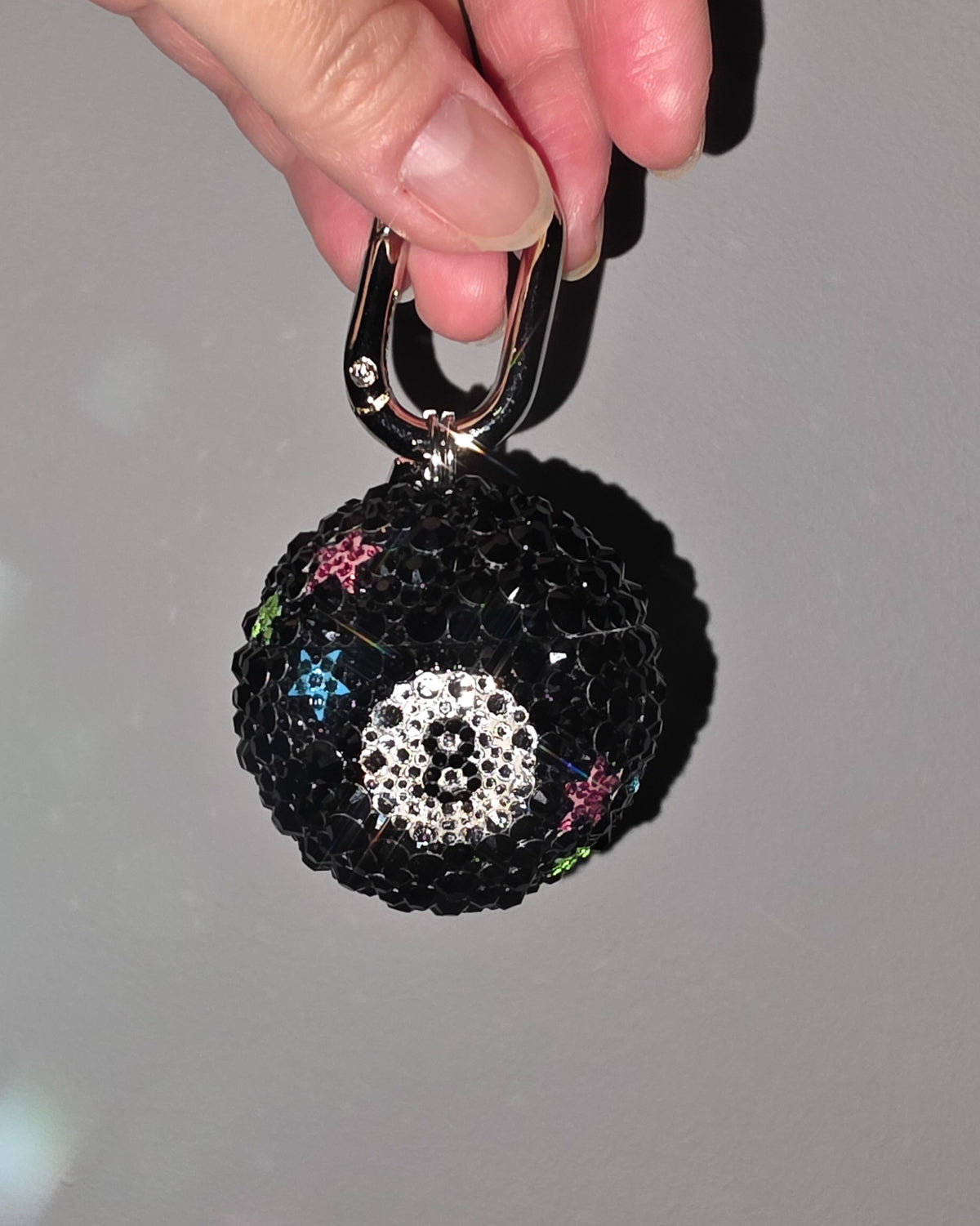 Black embellished keychain held by a hand against a gray background
