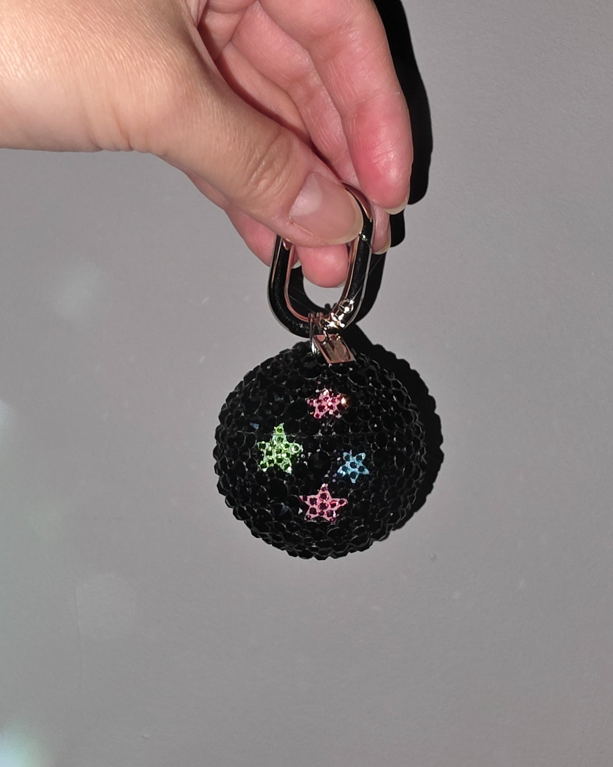 Black rhinestoned keychain with colorful star designs held by a hand against a gray background