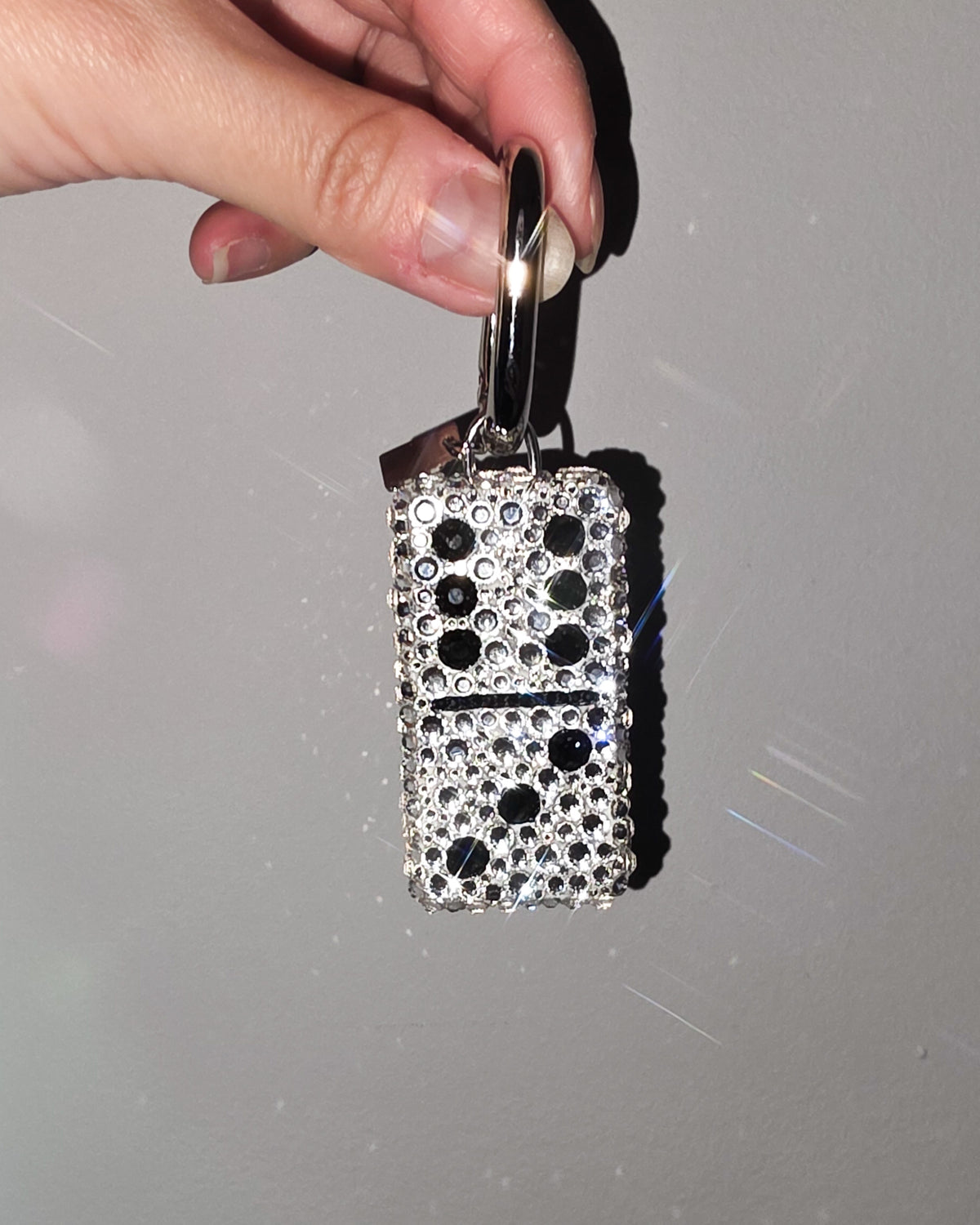 Hand holding a 6:3, fully rhinestoned domino bag charm against a gray background.
